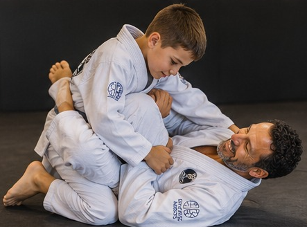 Black-and-white photo of a parent and child sitting together on the Jiu-Jitsu mat, warm and unposed
